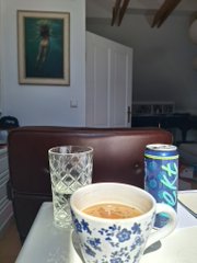 A patterned cup of coffee and an empty glass sit on a table, with a water bottle in the background. The image doesn't directly reference the crypto art purchase, serving instead as a relaxed café setting for this reflection on a low-cost NFT transaction.