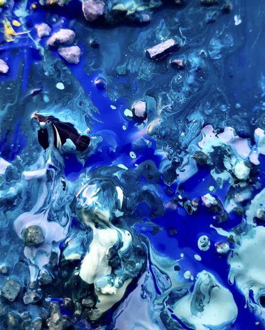 An abstract fluid art piece featuring swirling patterns of deep blue, white, and metallic colors with textured rock-like elements scattered throughout.