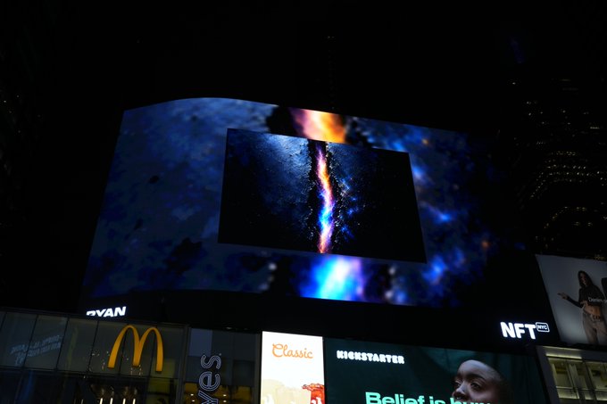 A nighttime urban scene showing a digital billboard displaying colorful abstract imagery, with visible signage for Ryan, NFT, McDonald's golden arches, 'Yes', Elclasico, and KICKSTARTER in the brightly lit commercial area.