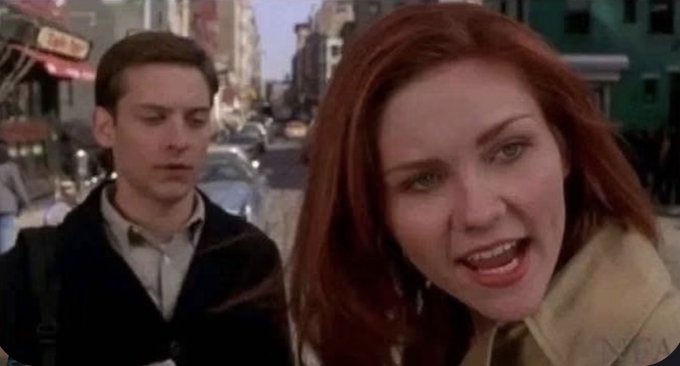 A movie still featuring Tobey Maguire's Peter Parker and Kirsten Dunst's Mary Jane Watson talking on a city street, from the Spider-Man film.