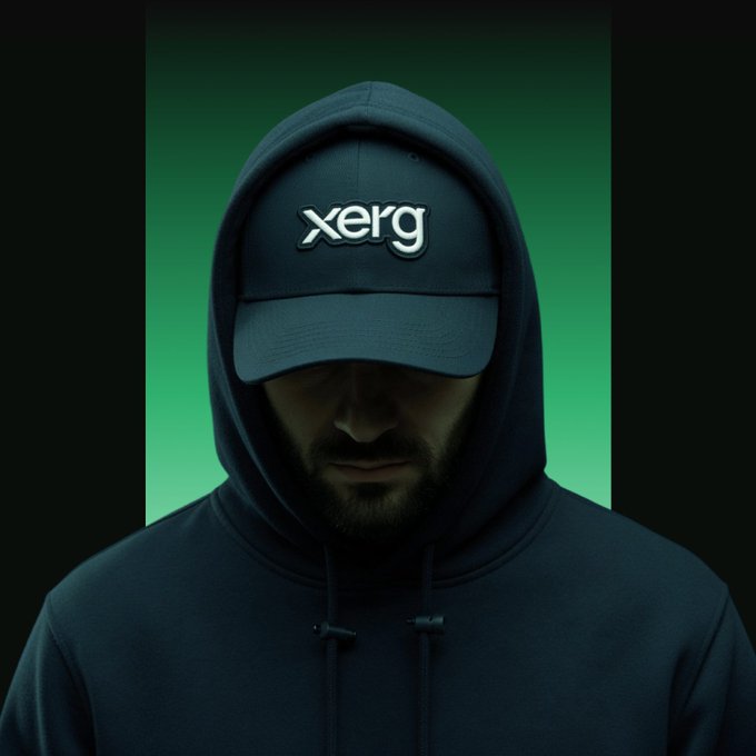 Mysterious portrait of a bearded man in a dark hoodie wearing a navy cap with the text 'xerg' on it, set against a green gradient background.