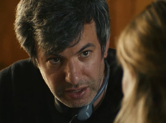 A man with dark, wavy hair leans in intensely, wearing what appears to be a stethoscope around his neck, gazing at a blonde person whose back is to the camera. The post humorously relates to the image by suggesting an absurd proposal—attaching eBay shares to GameStop warrant exercises—playing on the man's serious, focused expression as if diagnosing a wild financial scheme.