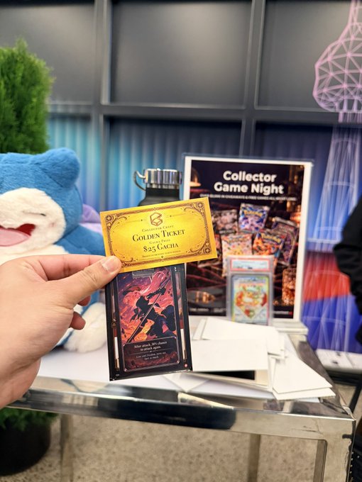 A hand holding a golden 'Golden Ticket' valued at $25 Gacha in front of a Snorlax plushie and a Collector Game Night display.