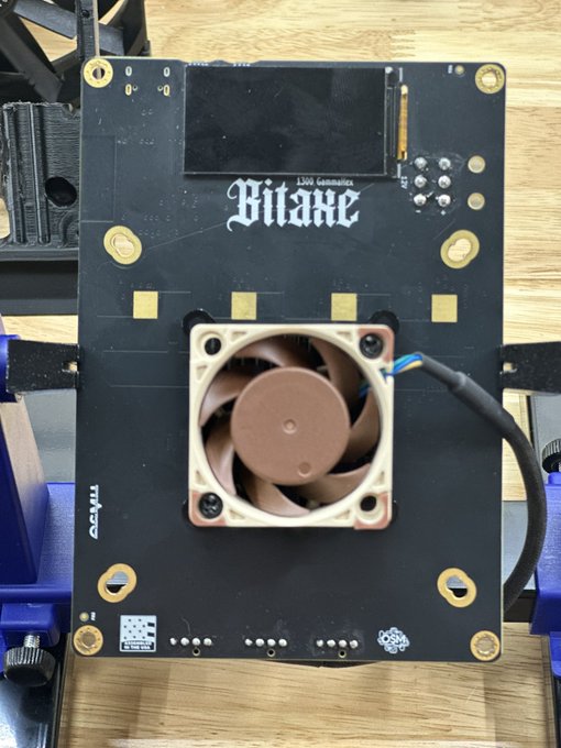 A black circuit board labeled 'Bitaxe' with a Noctua fan mounted in the center, appearing to be an open-source Bitcoin mining device.