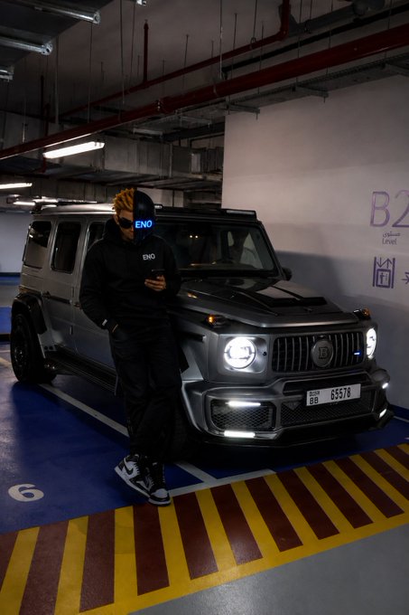 A person wearing an "ENO" branded mask and hoodie leans against a gray Mercedes-Benz G-Wagon (license plate "BB 65578") in a parking garage marked "B2 Parking Level," embodying the post's motivational message about seizing a fresh new day with focus and ambition.
