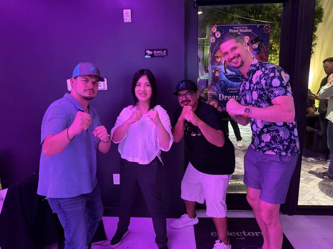 Four people pose playfully with raised fists in a purple-lit room, with one man wearing an 'LA' cap and another wearing an 'H' cap, standing near a poster mentioning 'Ponce Studios' and 'Dream'.