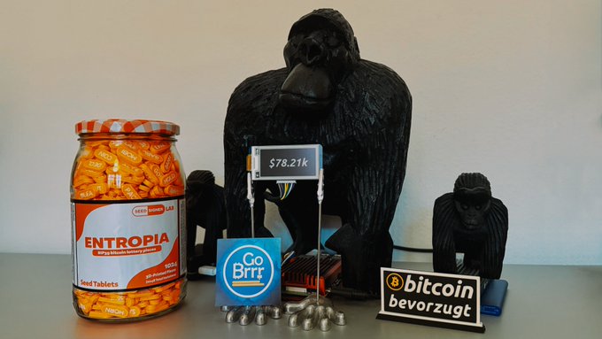 A humorous setup featuring a gorilla statue, a jar of 'Entropia' pills, a Bitcoin-preferred sign, and an electronic display showing $78.21k, with 'Go Brrr' signage.
