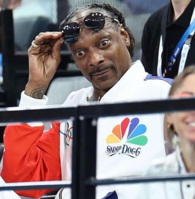 The image features a man wearing sunglasses, sitting down with his hand over his eye. The man appears to be looking at something or someone behind him, possibly a sports event or an advertisement related to the post. The background of the image shows other people in the scene, but they are not the main focus of the photo.