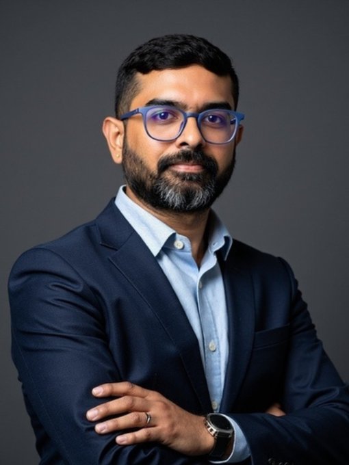 A professional headshot shows a man with a beard and glasses, wearing a navy blue blazer over a light blue shirt, with arms crossed and a smartwatch visible. The image accompanies the announcement of Arjun Balraj joining Preferrd as Fractional CTO, presenting a polished portrait that reflects his leadership role as an experienced technology executive.