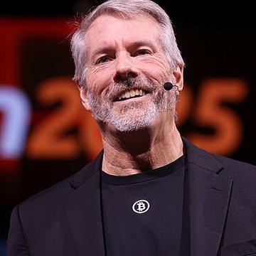 Michael Saylor smiles while speaking on stage, wearing a black t-shirt with a Bitcoin logo, in front of a backdrop displaying "2025." The image accompanies his statement about Bitcoin's breakthrough in converting economic energy into digital form.