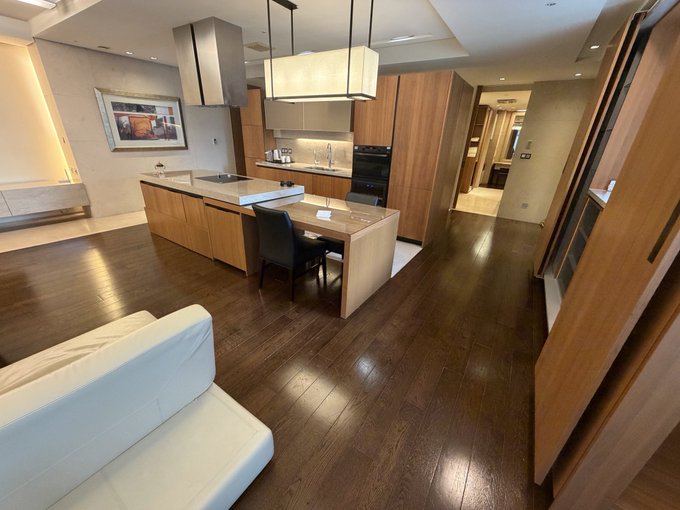 A spacious, modern open-plan kitchen and living area with dark hardwood floors, wood cabinetry, a large island with built-in stovetop, and a white sofa, photographed from an elevated angle—showcasing the roughly 120 sqm "runway-style" apartment layout mentioned in the post.