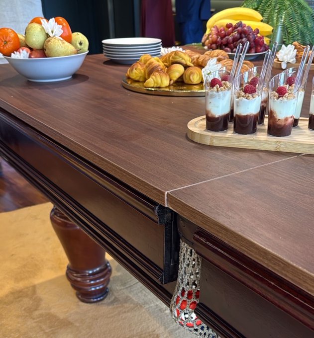 A luxurious breakfast spread featuring fresh fruit, pastries, and layered yogurt parfaits with raspberries is elegantly displayed on a polished wooden buffet table, fitting a cheerful "gm" (good morning) post. The rich breakfast offerings pair perfectly with the warm, welcoming morning vibe.