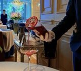 A person's hand holds a small red cylindrical can pouring a light-colored beverage into a clear glass on a counter.