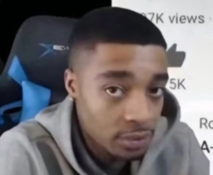 A young man wearing a gray hoodie sits in a gaming chair with a serious expression, in front of a background showing view counts like '7K views' and '5K'.