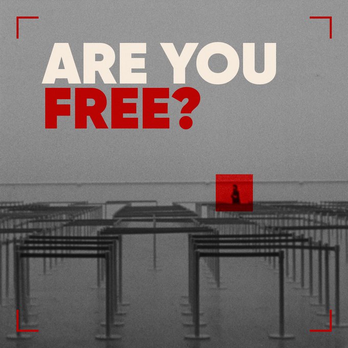 A grayscale graphic design with red accents asking 'ARE YOU FREE?' in bold text, showing a figure walking through what appears to be empty goalpost-like structures, framed by red corner brackets resembling a camera viewfinder.