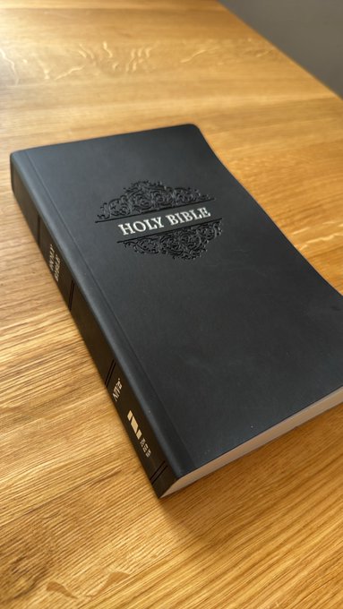 A black hardcover Holy Bible rests on a wooden surface, with its title embossed on the front cover and spine, complementing the post's recommendation to read the book of John.