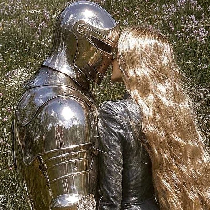 A whimsical image shows a knight in shining silver armor kissing a woman with long blonde hair in a field of white and purple wildflowers.