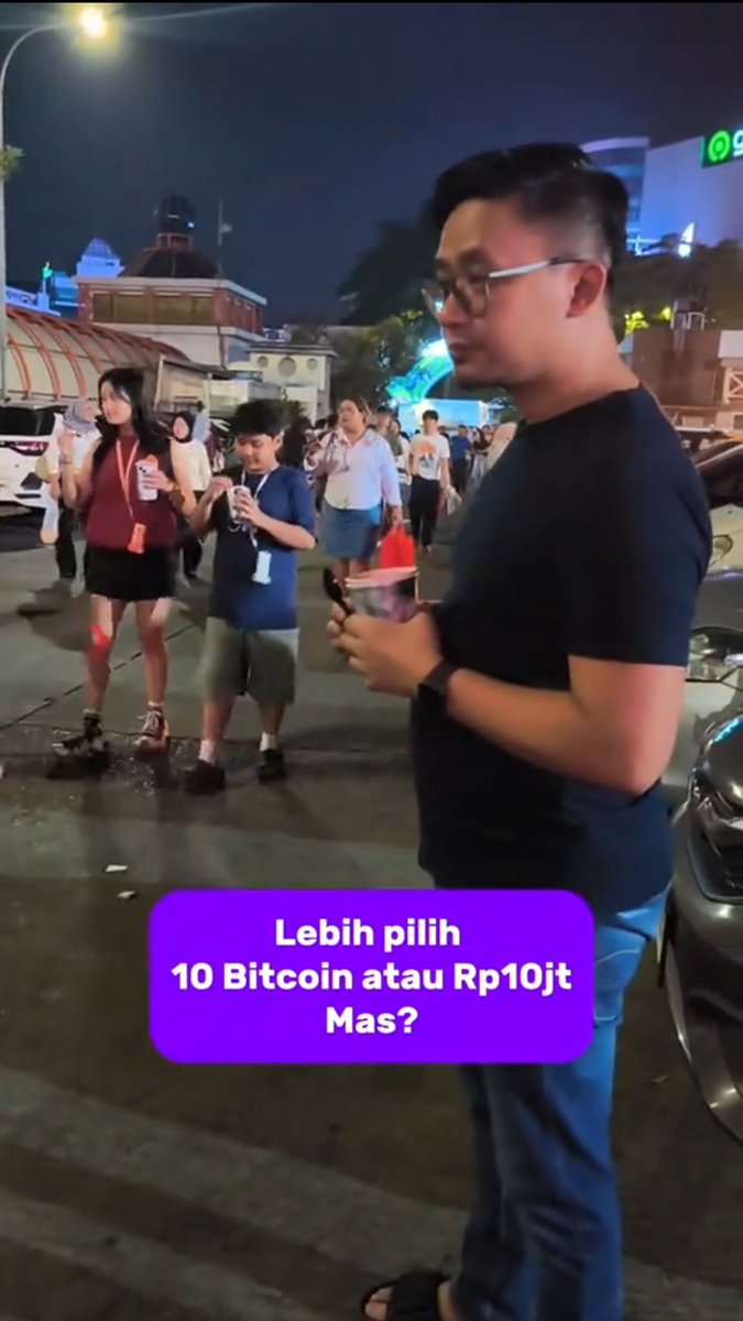 A man in glasses and a navy shirt stands on a nighttime street holding a phone, while a purple text box asks "Lebih pilih 10 Bitcoin atau Rp10jt Mas?" ("Which do you prefer, 10 Bitcoin or 100 million rupiah?"), prompting viewers to confront how Bitcoin's massive value appreciation makes the seemingly obvious answer of cash a costly mistake.