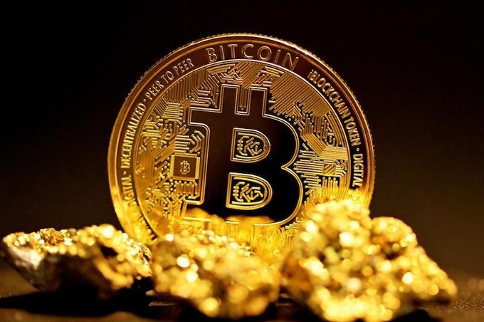 A close-up photograph of a golden Bitcoin coin resting on gold nuggets with text including 'BITCOIN', 'DIGITAL', 'DECENTRALIZED', 'PEER TO PEER', and 'BLOCKCHAIN TOKEN'.