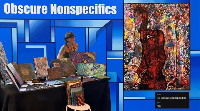An artist wearing a hat displays colorful abstract paintings at a booth titled 'Obscure Nonspecifics' with a featured piece titled 'roar' on the right.