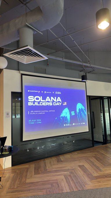 A projector screen displays "SOLANA BUILDERS DAY" event details at the Jelawang Capital Office in Kuala Lumpur, scheduled for 28 July 2025, 11AM-3PM, setting the scene for the Solana builders gathering at ILHAM Tower KL.