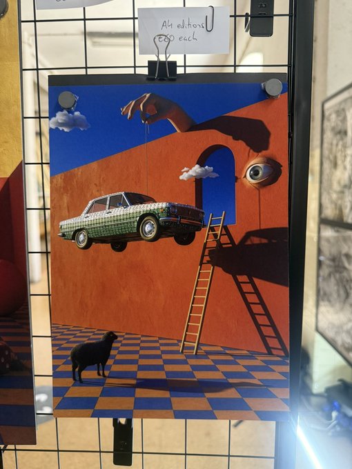 The image features an art piece that depicts a car with a ladder on top of it, creating an illusion as if the car is flying through the air. The painting is displayed on a wire rack or display board, which is mounted on a wall. The artwork has been edited and enhanced to make it appear more realistic by adding elements such as shadows and reflections. The post accompanying this image reads: "So I did a thing Got my print".
