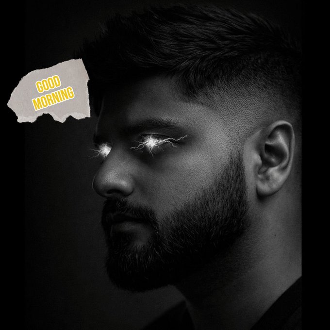 The image features a man with a beard, wearing a black shirt, looking at the camera. The background of the photo is black, which contrasts with the white paper that has "Good morning" written on it above the man's head. The text appears to be in yellow and orange colors, adding a pop of color to the image.