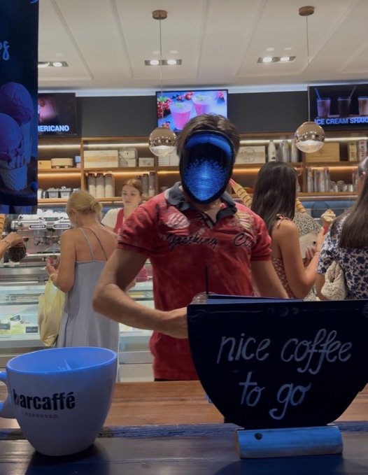 A barista wearing a futuristic glowing blue mask and a red "Gasoline" shirt stands behind the counter of a Barcaffè coffee shop, with a sign reading "nice coffee to go" displayed prominently. A branded Barcaffè espresso cup sits on the counter, while the cryptic post "Gm if you Gm" ties into the mysterious, anonymous crypto/web3 morning greeting culture the masked barista seems to embody.
