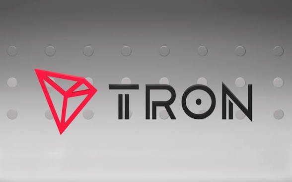 The TRON logo with its red diamond symbol is displayed against a gray, perforated metal background.
