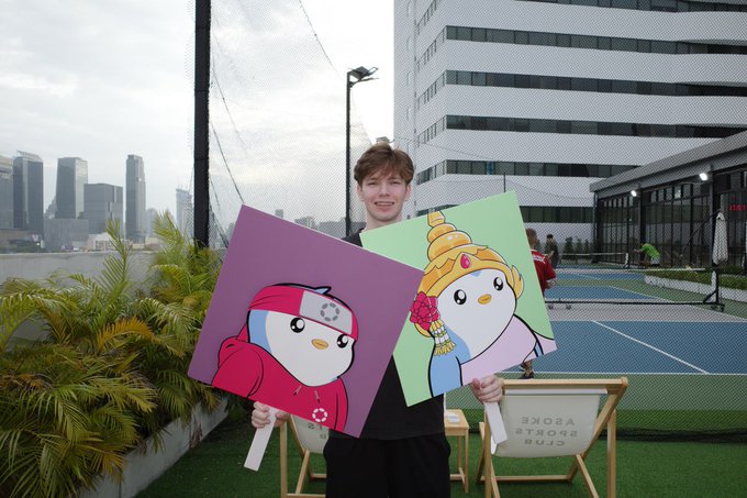 The image features a man holding two paintings of penguins, one purple and one green. The man appears to be posing for the pictures with these unique artwork pieces. The text "GM PENGUINS Are you still bullish on $PENGU" is present in the image, which seems to be related to the penguin paintings or possibly a conversation about them.

The post also mentions that there are two chairs and a dining table nearby, suggesting an outdoor setting for this artistic display. The man holding the paintings might be showcasing his interest in these unique artworks or discussing their value with someone else present at the location.