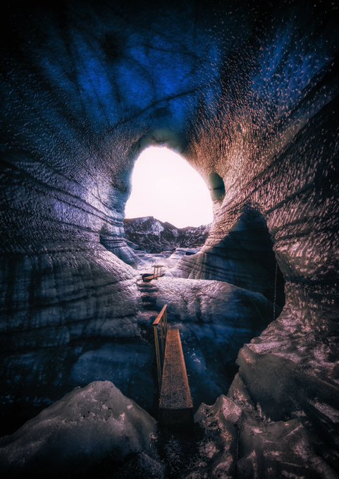 A wooden walkway leads through a luminous blue ice cave toward a bright archway opening, evoking a sense of awe and timelessness that mirrors the artwork's theme of "The Scale of Time" as a 1/1 NFT on SuperRare.