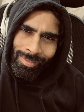 A bearded man wearing a black hoodie and white over-ear headphones smiles at the camera, looking pleased with himself. His confident, slightly smug expression matches the post's claim of having created melodic techno music from Bitcoin price action data, suggesting creative satisfaction with his unusual artistic experiment.