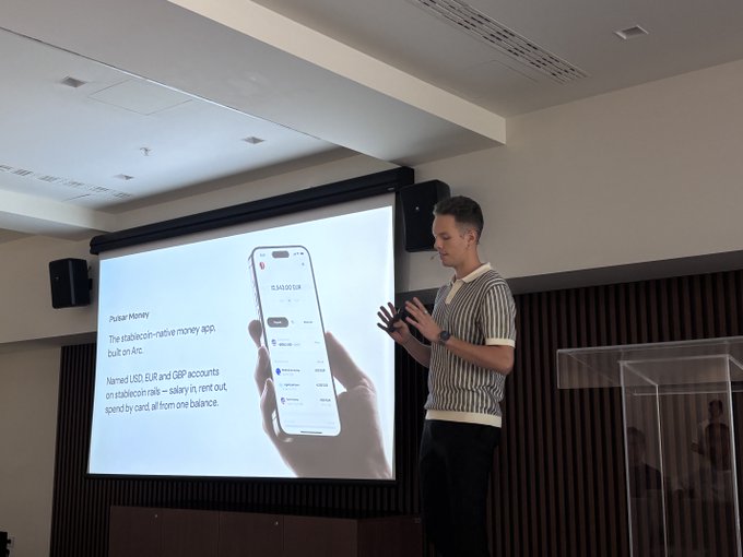 A man in a striped polo shirt presents "Pulsar Money," a stablecoin-native money app built on Arc, on stage at the EthBelgrade conference, displayed alongside a smartphone mockup showing a $3,163.00 EUR account balance.