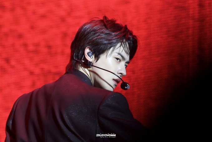 The image features a young man wearing headphones, possibly a singer or performer, with his back turned towards the camera. The background of the photo has a red hue, which could be an artistic choice or a stage lighting effect. The caption on the image reads "#LEO #이리오 파드라이브원 가져온 경우 구분자", which is likely a reference to the character Leo from the movie "Back to Back". The image also contains the text "ZDOWNSWORLDONE" and "ALPHADRIVEONE", possibly indicating that this photo was taken at a concert or event.