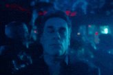 The image features a man with his eyes closed, sitting in front of a blue background that appears to be a city street at night. The man's face is partially visible behind him as he gazes into the distance. There are no other people or objects present in the image, and it does not contain any text.