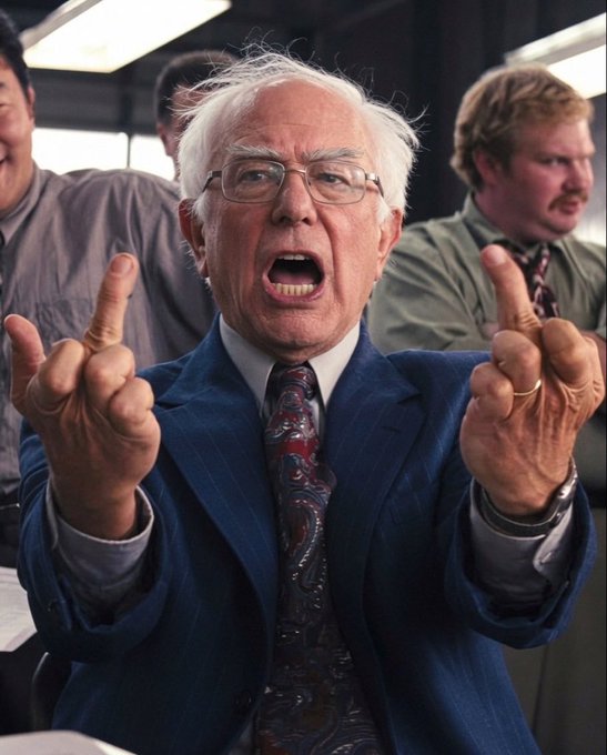 An older man with white hair in a blue pinstripe suit shouting angrily and pointing both index fingers forward, with other people visible in the background.