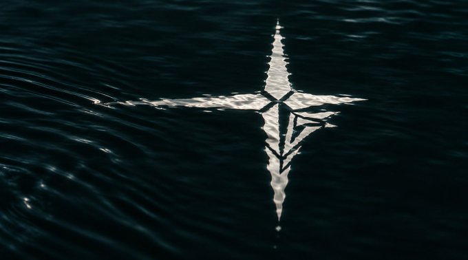 A dark, moody image shows a silver star and 'X' shape floating on the rippling surface of dark water.