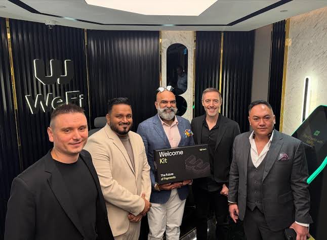 Five men pose together at the WeFi office, with one holding a "Welcome Kit: The Future of Payments" box beneath the company's branded wall logo, accompanying a post highlighting chairman Reeve Collins' extensive—but potentially overstretched—portfolio of leadership roles across WeFi, STBL Protocol, Pi Protocol, a crypto SPAC, and Fineqia.
