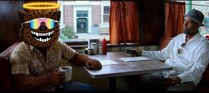 Two men sit across from each other in a diner booth; one has his face covered with a cartoon coyote wearing sunglasses and a halo, while the other wears a hat and holds a phone.