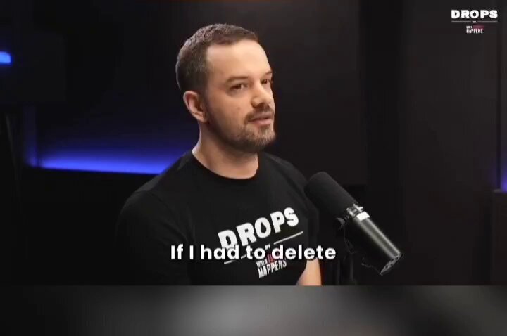 The image features a man wearing a black t-shirt with white text that says "drops" and "if i had". He is standing behind a microphone, suggesting he might be speaking or recording something. The background of the image is dark, which contrasts with the bright blue color in the top left corner. There are also some words written on the image, including "bitcoin", "buybacks", and "focus on what is in the image".