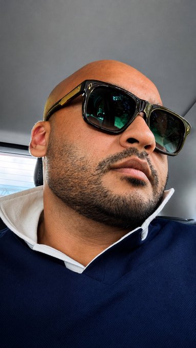 This is a close-up shot of a bald man with sunglasses and a beard, wearing a navy polo shirt. The image connects to the post by visually representing someone who might be considered a "millionaire" who understands the value of Bitcoin due to their existing problems and opportunities.