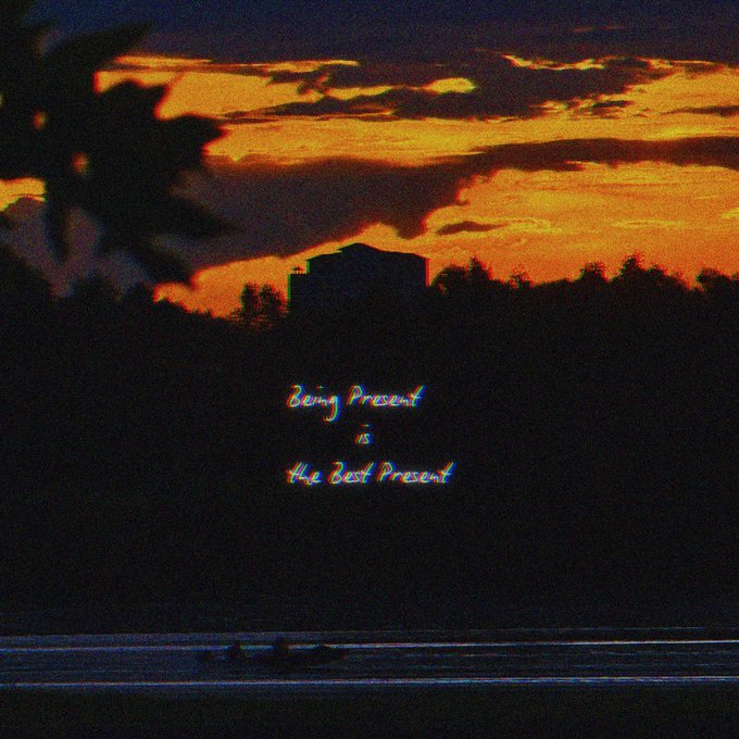 An atmospheric sunset photograph with dramatic orange clouds silhouetting trees and a building, overlaid with the inspirational quote 'Being Present is the Best Present' in stylized text.