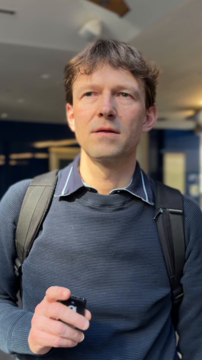 The image shows a man wearing a blue sweater, holding a cell phone, and looking up with an expression of surprise or confusion. The surrounding environment appears to be a hallway or corridor, which could be part of a school setting. The man's reaction suggests that he is surprised by something related to the content displayed on his cell phone screen. This might be an unexpected message, news article, or social media post about Bitcoin or cryptocurrency. It is important for children and young people to understand the basics of money management and financial literacy before they leave school, so they can make informed decisions about their finances in the future. The image serves as a reminder that staying updated with current events and understanding how technology impacts our lives is crucial for personal growth and development.