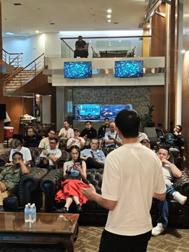 A presenter stands before an engaged audience seated on couches in a modern lounge, with digital displays and a TV visible in the background. The scene reflects the post's mention of a well-attended event highlighting OneSwap and CantonNetwork, suggesting this gathering took place before the next stop in Indonesia.