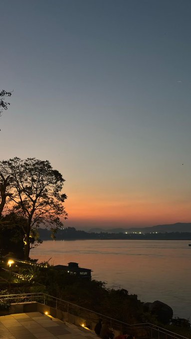 A twilight photograph shows a serene river view with a silhouetted tree and string lights on the left, under a gradient sky fading from blue to orange.