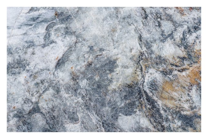A detailed close-up texture of a stone surface displaying a mix of white, grey, blue, and rust-orange veining and mottled patterns.