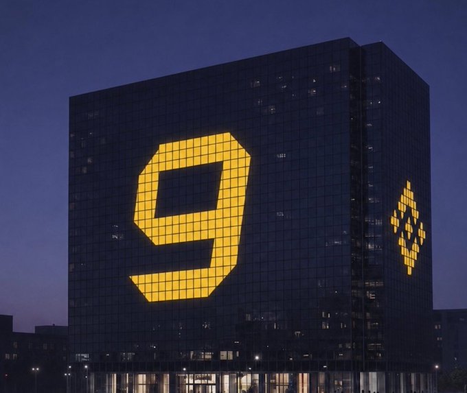 A tall building at night with a large illuminated yellow number '9' on its facade, along with a smaller logo on the side.
