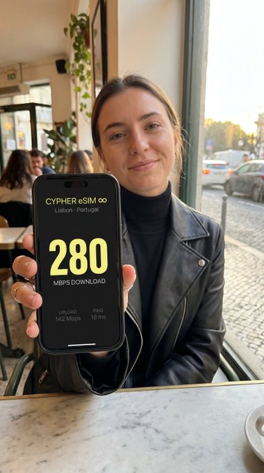 The image shows a woman sitting at a table with her cell phone held up next to her. The screen of the cell phone displays an advertisement for a new app called "CypherESIM" that offers faster, cleaner, and more private messaging services compared to traditional methods like Telegram or WhatsApp. The post also mentions five cryptos available on the app: Bitcoin, USDC, ETH, SOL, and XRP.