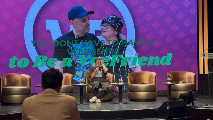 A stage presentation with a person speaking while seated, with on-screen text reading "YOU DON'T HAVE TO HAVE A WEIRD SIDE to Be a Yes Friend," set against a purple backdrop showing two people.