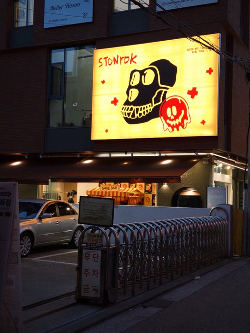 A nighttime street view of a Korean BBQ restaurant called 'STONROK' featuring a brightly lit yellow sign with a cartoon skull logo, with Korean text '무단 주차 금지' (No Unauthorized Parking) visible below.